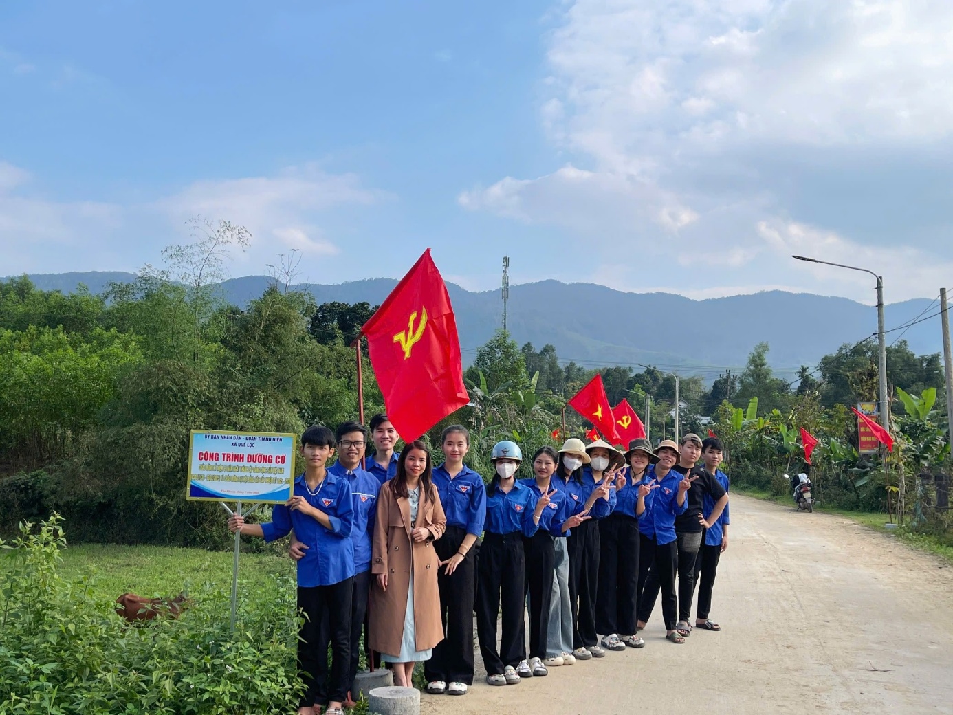 A group of people standing on a road with flags Description automatically generated