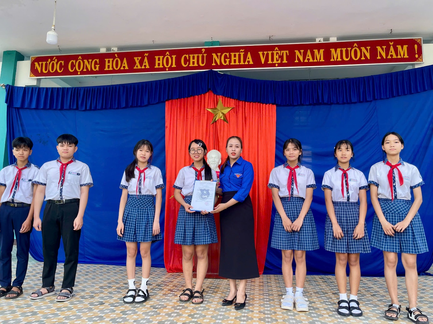 A group of people standing in front of a blue and red curtain Description automatically generated