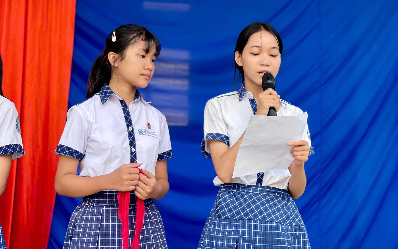 Two girls in matching outfits holding a microphone and a paper Description automatically generated